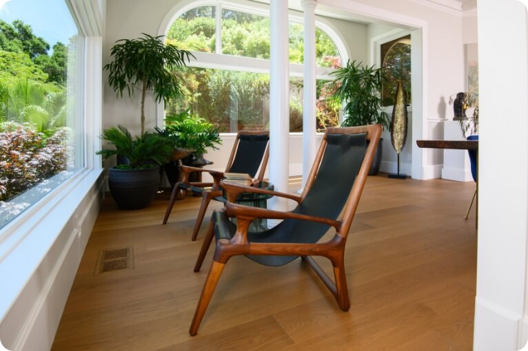 Stylish wooden chairs in a bright, modern living room with large windows and greenery.